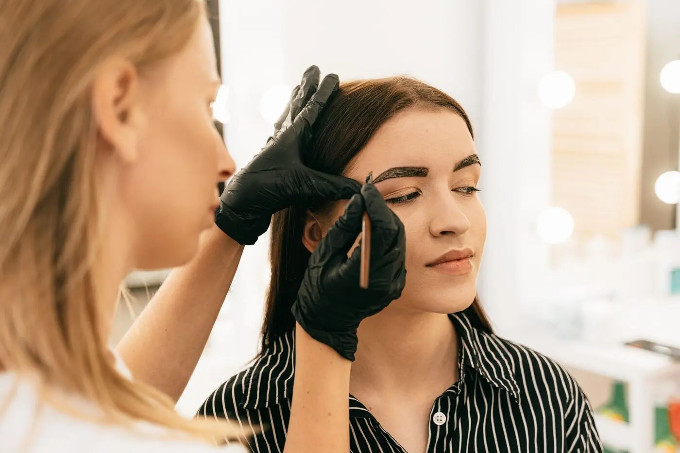 Brow artist shaping a client's eyebrows in a bright studio